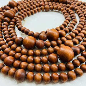 May include: Multiple strands of wooden beads in various sizes and shades of brown are arranged in a circular pattern. The beads vary from small, round shapes to larger, spherical beads. The beads are strung together, creating a natural, earthy aesthetic.