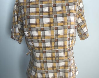 May include: A vintage short-sleeved top with a plaid pattern in shades of yellow, white, gray, and brown. The top has a boat neckline and a fitted silhouette. The fabric appears to be a woven material. The top is displayed on a mannequin.