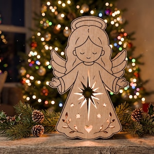 May include: A light-colored wooden angel cutout featuring a laser-cut star design at the center, a halo, and engraved details including small stars, leaves, and a heart. The figure is illuminated from within, casting a warm glow through the cutouts.