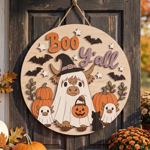 May include: A round wooden sign featuring the text Boo Y'all, a Highland cow wearing a witch hat and ghost sheet, two smaller ghost-covered cows, pumpkins, black bats, and white stars. The sign is suspended by a rope against a dark door.