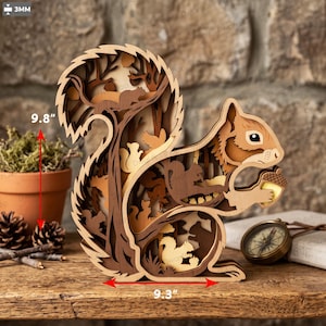 Puede incluir: Una escultura de ardilla de madera multicapa en varios tonos de marrón, que mide 24,9 cm de alto y 23,6 cm de ancho. El diseño incorpora recortes intrincados de ardillas y árboles, con la ardilla principal sosteniendo una bellota.