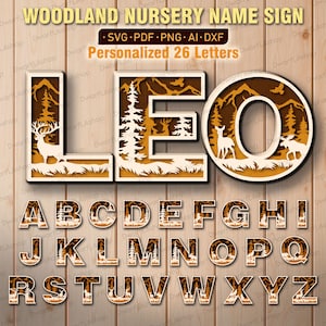May include: A personalized woodland nursery name sign with the name "LEO" displayed. The letters are brown and white, featuring a forest scene with deer and trees. The sign includes the full alphabet for customization.