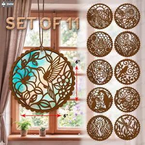 Op de afbeelding: Set van 11 houten decoratieve ornamenten. Een groot rond ornament met een kolibrie- en bloemmotief, 15 cm in diameter, hangt voor een raam. De andere 10 ornamenten hebben verschillende dieren- en natuurontwerpen.