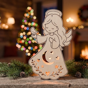 May include: A light-colored wooden cutout of an angel with a halo, long hair, and wings. The angel holds a small bird in one hand. The dress features cutouts of a crescent moon, several stars, a heart, and leafy vine patterns throughout.