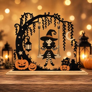 Pu&ograve; includere: Una decorazione in legno intagliato nero e arancione raffigurante una strega seduta su un'altalena appesa a un ramo. La scena include una luna crescente, stelle, una lanterna appesa, due zucche e un gatto nero con un cappello da strega.