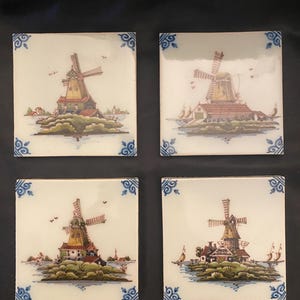 May include: Four square ceramic tiles with a Dutch windmill scene. Each tile features a detailed illustration of a windmill, with a red roof, set against a landscape with water and greenery. The corners have blue floral designs.