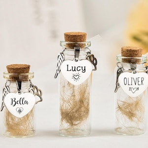 May include: Three small glass jars with cork tops, each containing a small amount of fur. Each jar has a silver heart charm with a name on it: Bella, Lucy, and Oliver. The charms also have small paw prints and a heart.