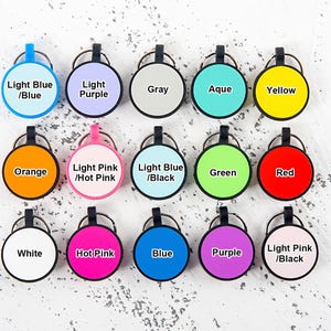 Puede incluir: Una colecci&oacute;n de quince etiquetas circulares para llaves dispuestas en tres filas, cada una con un borde negro, una anilla met&aacute;lica y un centro de color. Las etiquetas incluyen el texto Light Blue/Blue, Light Purple, Gray, Aqua, Yellow, Orange, Light Pink/Hot Pink, Light Blue/Black, Green, Red, White, Hot Pink, Blue, Purple y Light Pink/Black.