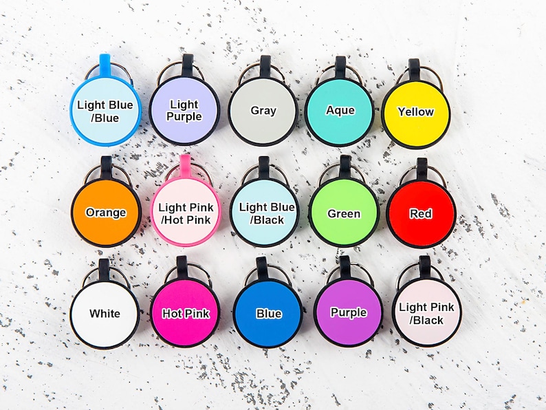 Puede incluir: Una colecci&oacute;n de quince etiquetas circulares para llaves dispuestas en tres filas, cada una con un borde negro, una anilla met&aacute;lica y un centro de color. Las etiquetas incluyen el texto Light Blue/Blue, Light Purple, Gray, Aqua, Yellow, Orange, Light Pink/Hot Pink, Light Blue/Black, Green, Red, White, Hot Pink, Blue, Purple y Light Pink/Black.