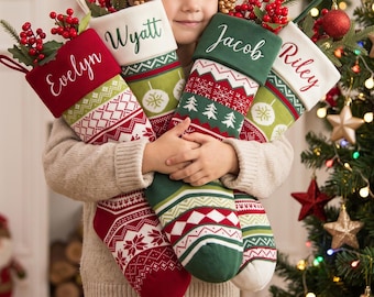 May include: Four personalized Christmas stockings featuring red, green, and white knit patterns. The stockings are embroidered with the names Evelyn, Wyatt, Jacob, and Riley on the cuffs and are filled with artificial red berry sprigs.