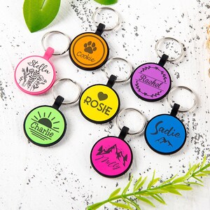 Puede incluir: Una colecci&oacute;n de siete llaveros circulares en varios colores, incluyendo rosa, naranja, amarillo, morado, verde, azul y rosa intenso. Cada llavero cuenta con una anilla met&aacute;lica y un dise&ntilde;o gr&aacute;fico negro &uacute;nico con nombres como Stella, Cookie, Rosie, Rachel, Charlie, Milly y Sadie.