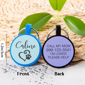 Puede incluir: Dos placas de identificaci&oacute;n circulares para mascotas de 3 cm de di&aacute;metro. La azul muestra el nombre Caline y un coraz&oacute;n con una huella. La negra incluye el texto CALL MY MOM, 999-123-3541, I'M LOVED!, PLEASE HELP. Ambas tienen anillas met&aacute;licas.