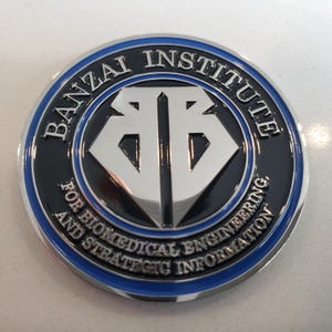 May include: A round, silver coin with a blue border. The coin has a black center with a silver logo of two interlocking Bs. The text "BANZAI INSTITUTE FOR BIOMEDICAL ENGINEERING AND STRATEGIC INFORMATION" is written around the border.