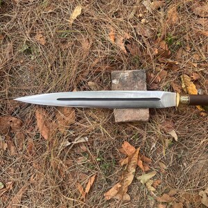 May include: A long, silver-colored sword with a brown handle and gold accents. The sword is lying on a bed of brown leaves.