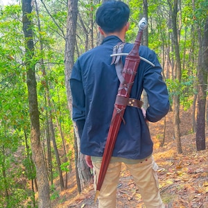 May include: A person wearing a blue shirt and khaki pants is wearing a brown leather sword scabbard with a silver sword strapped to their back.