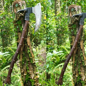 May include: A large, curved axe with a dark wood handle and a silver blade. The axe is leaning against a tree trunk covered in moss and mushrooms.