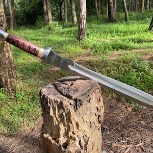 May include: A silver and brown sword with a wooden handle rests on a tree stump. The sword has a long, double-edged blade and a decorative handle with a silver pommel and a brown grip.