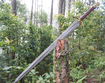 May include: A silver sword with a brown wooden handle and gold accents. The sword is resting on a tree stump in a forest setting.
