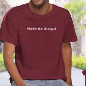 May include: A maroon t-shirt with white text that reads "Member of an elite squad".