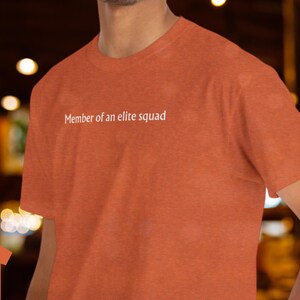 May include: A rust orange t-shirt with the text "Member of an elite squad" printed in white on the front.