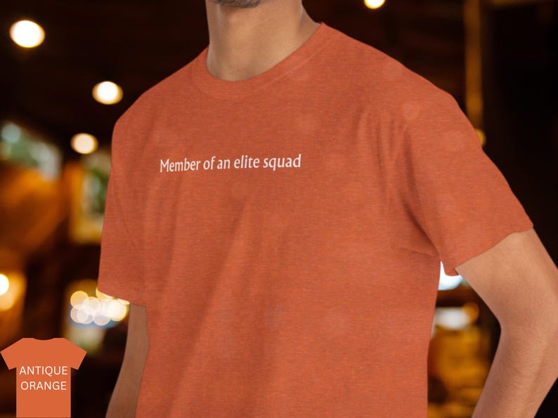 May include: A rust orange t-shirt with the text "Member of an elite squad" printed in white on the front.