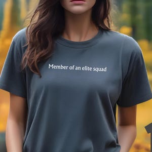 May include: A dark heather grey t-shirt with the text "Member of an elite squad" printed on the front.