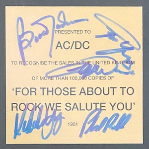 May include: A tan certificate featuring blue signatures and text. The text states "PRESENTED TO AC/DC" and "FOR THOSE ABOUT TO ROCK WE SALUTE YOU". It acknowledges sales in the United Kingdom exceeding 100,000 copies. The year 1981 is also displayed.