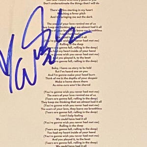 Puede incluir: Una hoja de papel blanca con letras de canciones impresas y una firma azul. Las letras están en fuente negra y la firma en tinta azul. El papel es ligeramente blanquecino, con una firma grande y prominente.