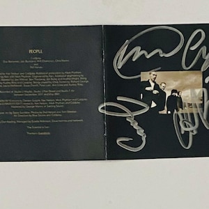 May include: A black and white photo of a band, People, on a black CD cover. The band members are standing in a row, and the cover is signed in silver marker.