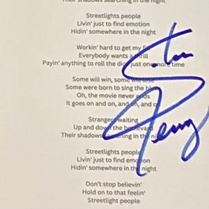 Puede incluir: Un papel blanco con letras de canciones y una firma azul. Las letras incluyen frases como "Streetlights people" y "Don't stop believin'". La firma está en tinta azul.