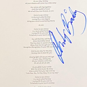 Pode incluir: Uma folha de papel branco com a letra impressa em preto da música Fantasy, incluindo linhas como On our ship, fantasy e All your dreams will come true. Uma assinatura em tinta azul está escrita verticalmente no lado direito da folha.