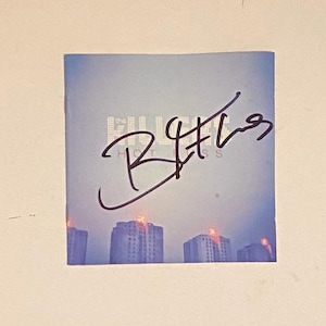May include: A signed CD by The Killers, titled "Hot Fuss". The CD cover features a blue and purple sky with a cityscape in the background. The signature is in black ink.