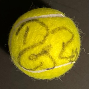 May include: A bright yellow tennis ball with a white seam. The ball has dark markings on its surface. The tennis ball is a standard size for the sport.