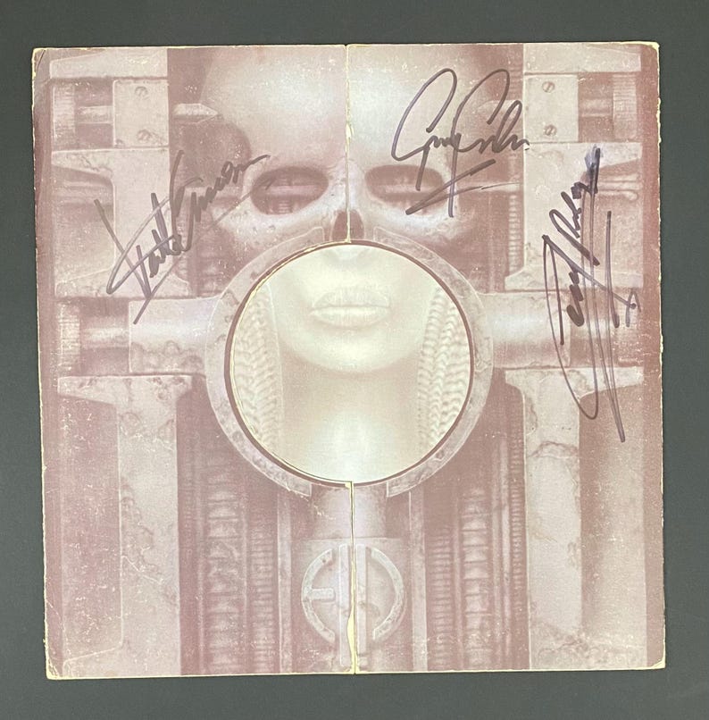 May include: Album cover with a surreal, sepia-toned image featuring a human face within a circular frame, surrounded by mechanical structures. The cover is signed by multiple people. The overall theme is science fiction.