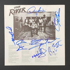 以下が含まれることがあります： 「The River」のヴィンテージアルバムカバー。バンドの写真と青インクの手書きサイン入り。セピア色のカバーには、木製のデッキに立っているバンドが写っています。