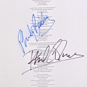 Può includere: Un foglio di carta bianca con il testo stampato in nero della canzone Easy Lover, sovrapposto a due firme distinte. Una firma è scritta con inchiostro blu, mentre la seconda firma è scritta con inchiostro nero al centro del testo.
