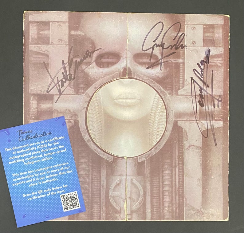 May include: A signed album cover featuring a surreal, biomechanical artwork in shades of brown and beige. The cover has multiple signatures and a blue Thorne Authentication certificate with a QR code.