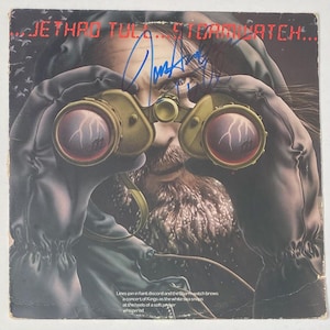 Può includere: Una copertina di un album in vinile vintage con un uomo barbuto che guarda attraverso un binocolo. La copertina dell'album è per la band Jethro Tull e l'album si chiama "Stormwatch".