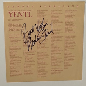 Könnte beinhalten: Ein Vintage-Schallplattencover für den Soundtrack zum Film "Yentl" mit Barbra Streisand. Das Albumcover zeigt den Filmtitel und eine Liste von Songtiteln. Das Album ist von Barbra Streisand und dem Komponisten Michel Legrand signiert.