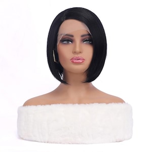 May include: A mannequin head with a black bob wig. The wig features a side part and a lace front. The mannequin is wearing gold hoop earrings and has full makeup. The mannequin is resting on a white, fluffy, off-the-shoulder garment.