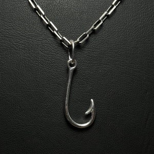 Può includere: Una collana a catena d'argento con un ciondolo a forma di amo da pesca in argento.