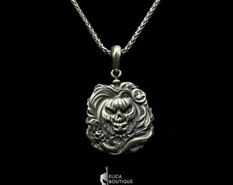 May include: A silver necklace with a detailed pendant featuring a carved pumpkin face with a menacing expression. The pendant is surrounded by intricate floral designs.