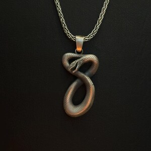 Op de afbeelding: Een zilveren slangenhangerketting met een gevlochten ketting. De slang is opgerold in een oneindigheidssymbool.