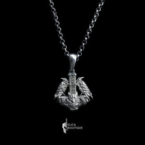 May include: A silver necklace with a pendant featuring a detailed design of a hammer with two ravens perched on top. The pendant is intricately crafted with a woven pattern and a wolf's head at the base.