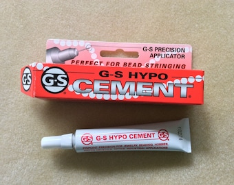 May include: A red and white tube of G-S Hypo Cement with a precision applicator. The tube is labeled "G-S Hypo Cement" and "Pinpoint Precision for Jewelry, Beading, Hobbies, Watch Crystals, Optics, Industrial Applications".