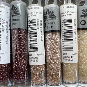 May include: Six tubes of TOHO Treasure seed beads in various colours, including gold luster, transparent amethyst, matte silver-lined Rosaline, and Ceylon light ivory. Each tube is labelled with size #1 and contains approximately 8.9 grams of beads.