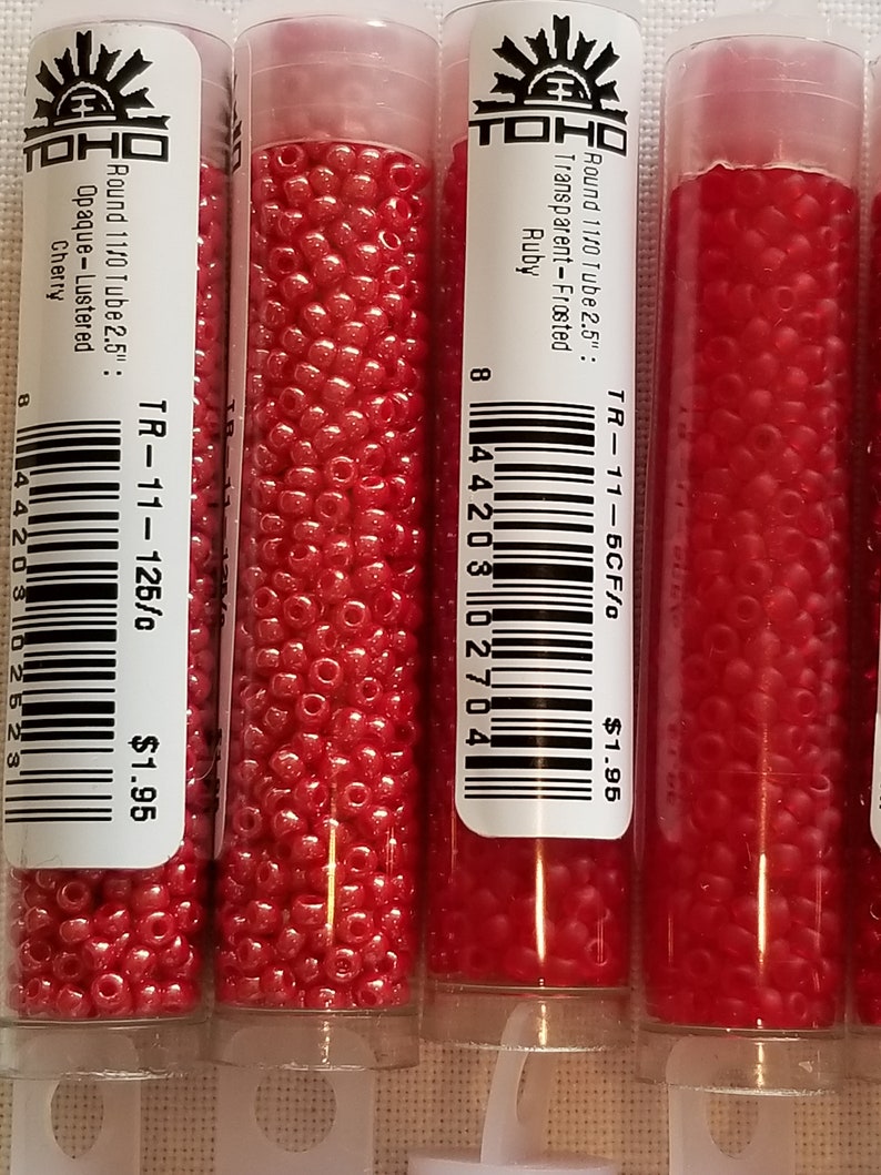 Pode incluir: Tr&ecirc;s tubos de contas de sementes vermelhas TOHO. Os tubos s&atilde;o etiquetados com o tamanho da conta, a cor e o acabamento. Os tubos s&atilde;o etiquetados "Round 11/0 Tube 2.5": Transparent-Frosted Ruby", "Round 11/0 Tube 2.5": Opaque-Lustered Cherry", e "Round 11/0 Tube 2.5": Transparent-Frosted Ruby". Cada tubo custa &euro; 1,95.