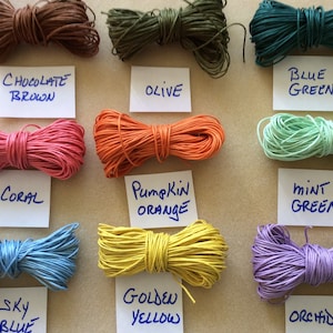 May include: Assortment of 10 spools of waxed cotton cord in various colors, including chocolate brown, olive, blue green, coral, pumpkin orange, mint green, sky blue, golden yellow, and orchid. Each spool is labeled with the color name.