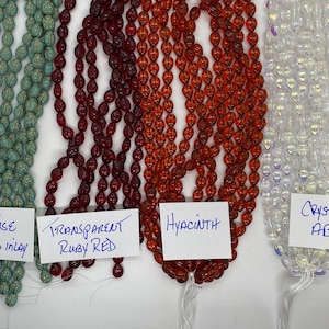 May include: Four strands of glass beads in different colors. From left to right: turquoise with gold inlay, transparent ruby red, hyacinth, and crystal AB.