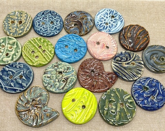 Könnte beinhalten: Sortiment von 16 handgefertigten Keramikknöpfen in verschiedenen Farben und Mustern, darunter Blau, Grün, Braun, Gelb und Rosa. Die Knöpfe haben eine Vielzahl von Designs, wie z. B. Blumen, geometrische und abstrakte.